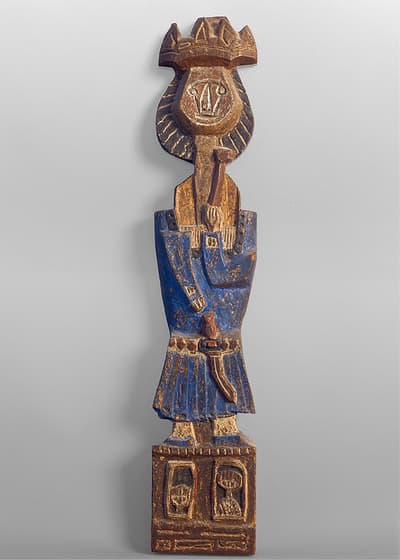 A wooden carved figure in a blue robe with a crown, standing on a decorated base.