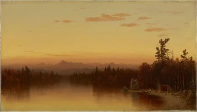 A sunset over a forested lake with distant mountains and a warm, glowing sky.