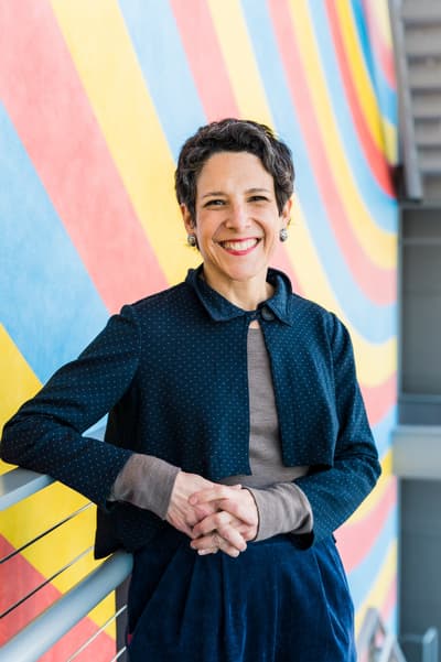 Portrait of Jacqueline Terrassa, Carolyn Muzzy Director in front of a colorful wall work by artist Sol LeWitt