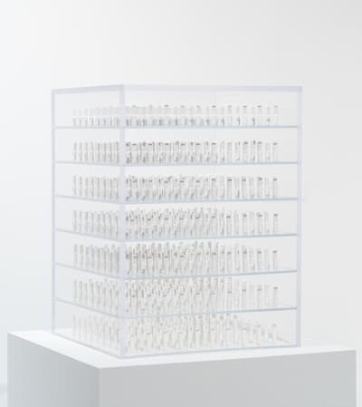 A clear display case with six sections filled with rolled white items on a white pedestal.