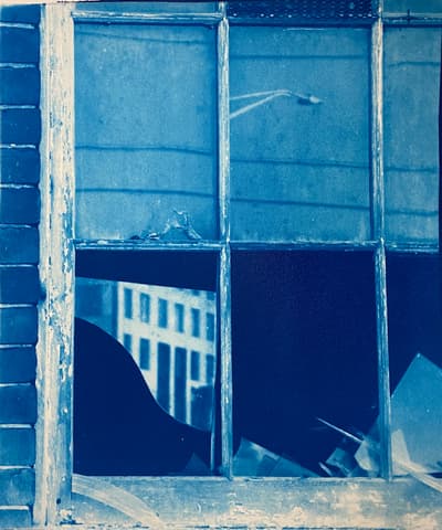 A cyanotype print of a broken window with reflections of building and traffic lights.
