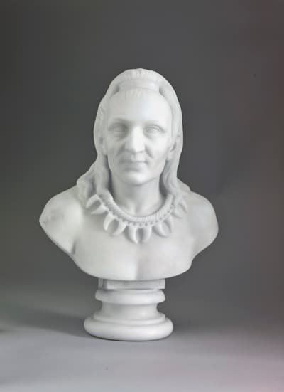 White marble bust of a figure with long hair and a decorative necklace on a cylindrical pedestal.