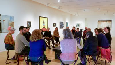 Group of people seated in circle in a gallery speaking to one another