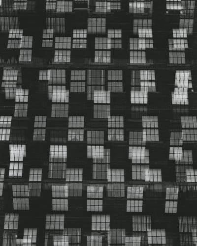 Abstract pattern of white-framed windows on a dark brick building façade.