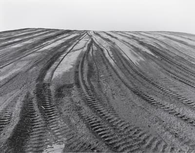 Black and white photo of parallel tire tracks on barren soil.