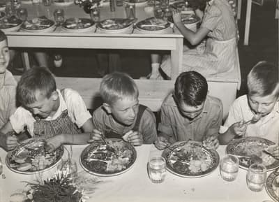 Young boys eating at a table with decorative plates and glasses, in a black and white setting.