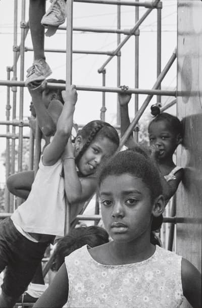 Children playing on a metal jungle gym, with one girl in the foreground facing the camera.
