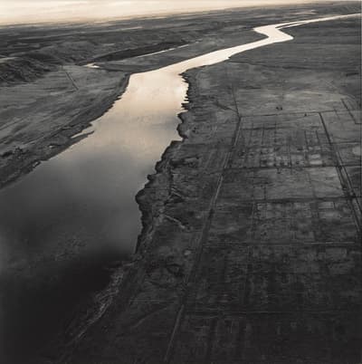 Aerial view of a river winding through a barren landscape, with grid-like patterns on the right side.