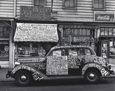 A black and white photo of a text-covered car parked in front of a liquor store with various signs.