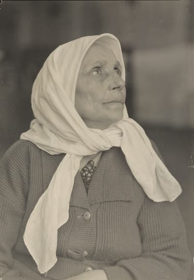 Black-and-white portrait of an elderly woman with a white headscarf, looking upwards.
