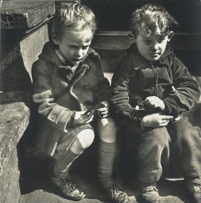 Two children sitting on stone steps, holding objects. Black and white photograph.