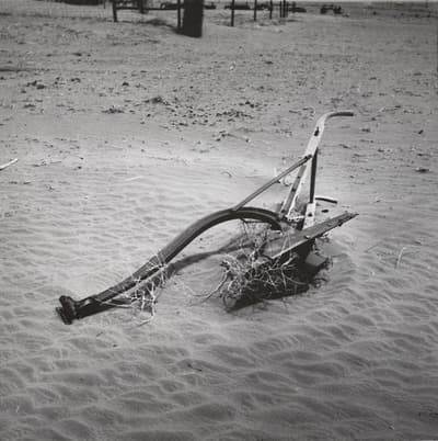 A rusted plow partially buried in a sandy landscape.