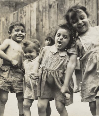 Four children smiling and playing in front of a wooden fence.