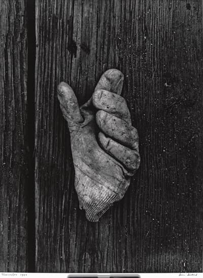A dirty work glove hanging from a wooden plank.