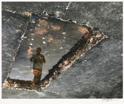 Reflection of a person in a puddle on a concrete surface.