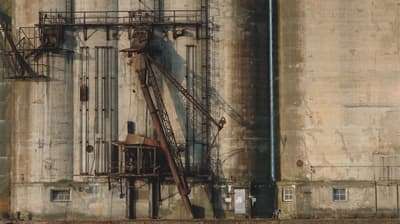 Weathered industrial facility wall with rusty metal structures and concrete surfaces.