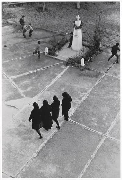 Aerial view of a concrete courtyard with four women in dark clothing and children playing near a monument.