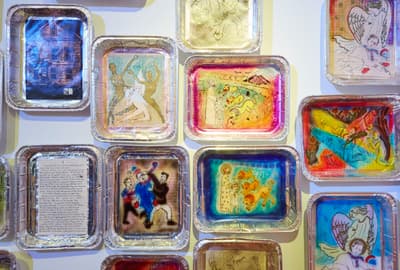 A grouping of more than a dozen small paintings inside aluminum baking tins displayed salon style by Thomas Lanigan-Schmidt.