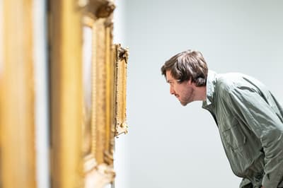 A man bends down to look closely at a painting