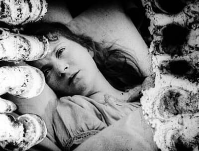A woman lying in bed with textured cylindrical shapes in the foreground.