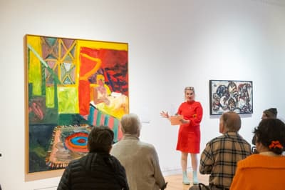 Curator gesturing to artwork in gallery in front of a group of visitors