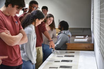 A group of students viewing Fourteen Etchings, a print portfolio by Terry Winters, placed on a table in the Landay Teaching Gallery