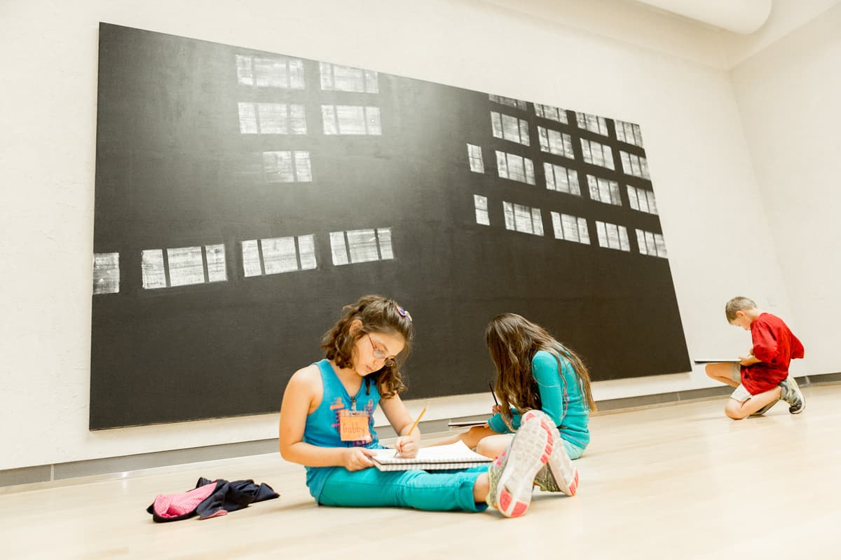 Three children with sketch books in front of painting