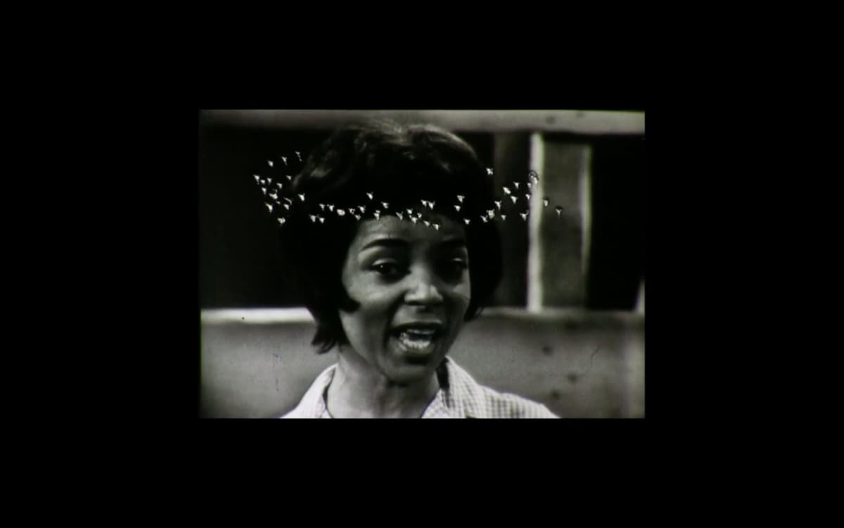 A video still of a woman who appears to be singing or speaking with white markings suspended around her head.