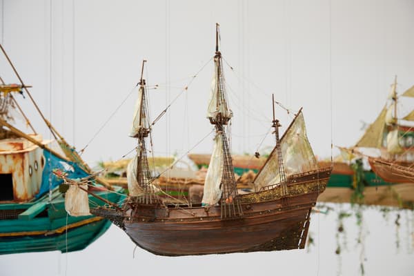 Detailed model of an old sailing ship against a white background with other ships visible in the distance.