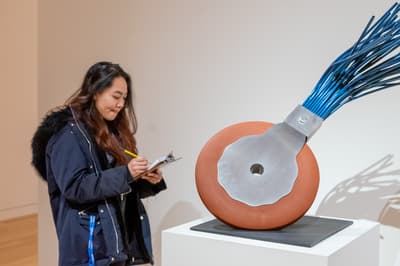 A student with a clipboard and pencil standing in front of a sculpture