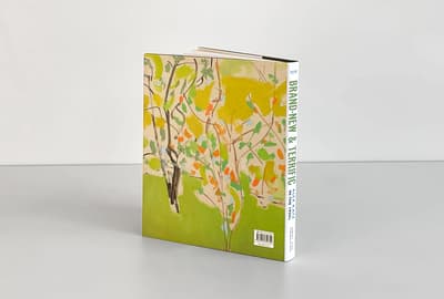A hardcover book titled "Brand-New & Terrific" by Alex Katz, featuring an abstract tree painting on the cover, stands upright against a gray background.