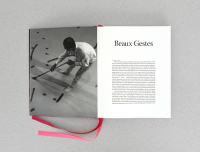 Open book showing a photo of a person with a stick and an article titled "Beaux Gestes."