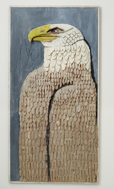A carved and painted wood bald eagle sculpture. The piece depicts the bird's proud-seeming profile.