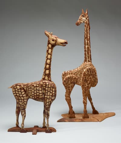 A pair of sculptures created from stained and painted wood depicting giraffes.