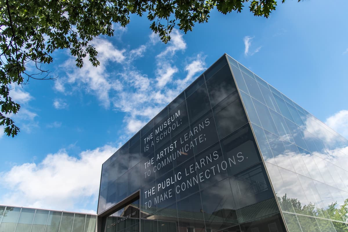 Photograph of the exterior of the museum. A text-based artwork is visible from the outside. It reads: The Museum is a School; The Artist Learns to Communicate; the Public Learns to Make Connections.