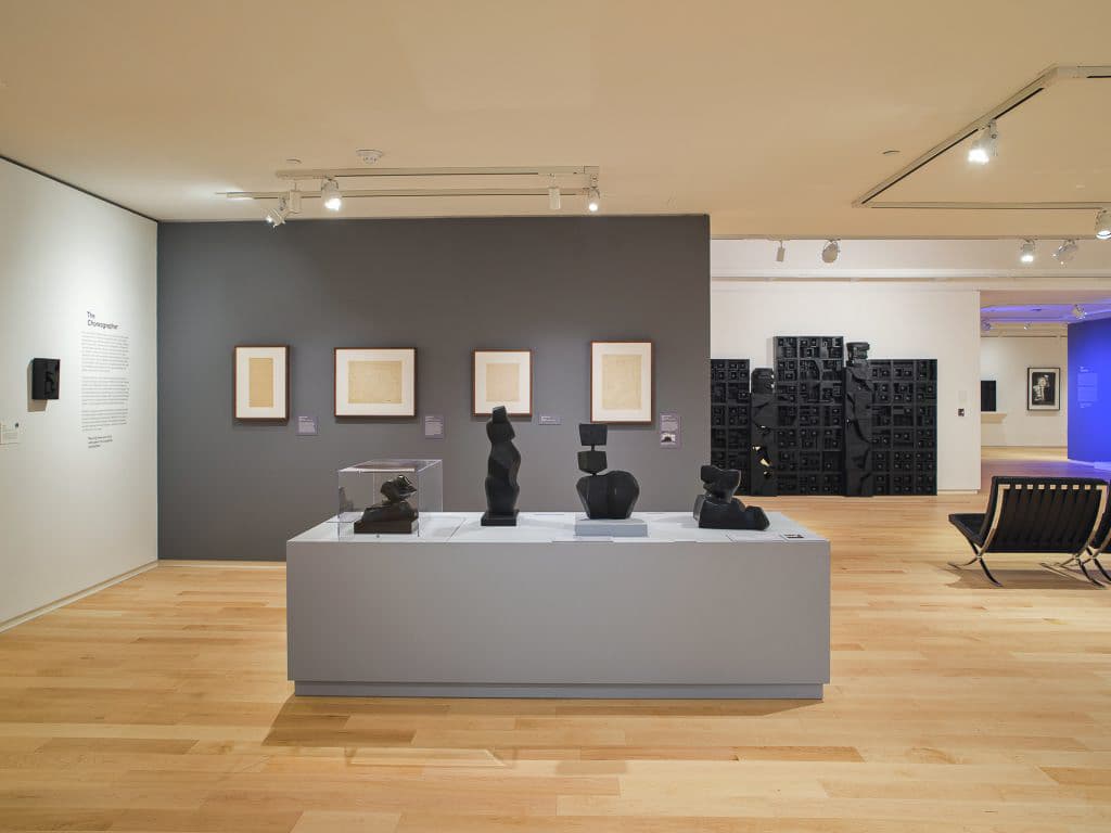 Art gallery interior with abstract sculptures and framed sketches.