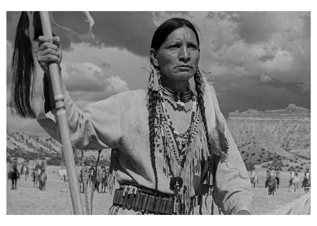 Person in traditional attire holding a staff with a natural backdrop.