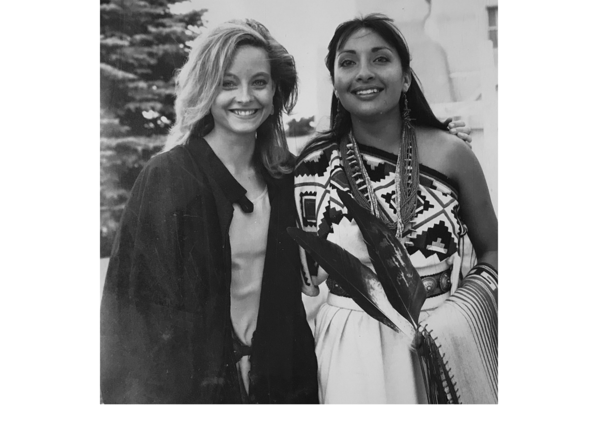 Two women smiling; one in modern clothing and the other in traditional attire with geometric patterns.