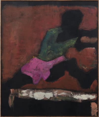 A dark figure in pink shorts and a green shirt jumping over a hurdle.