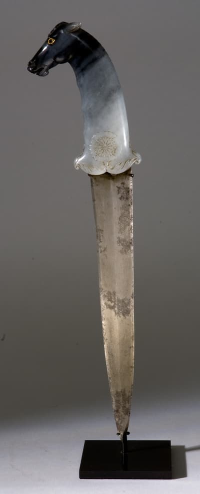 A knife with an intricately carved jade handle in the shape of a horse head.