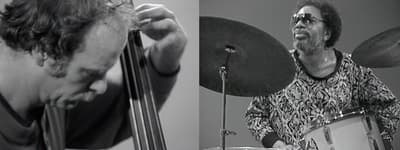 Still from two-channel video showing a bass player on the left and a drummer at a drum kit on the right.