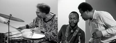 Still from two-channel video showing a drummer in motion and one musician speaking to another.