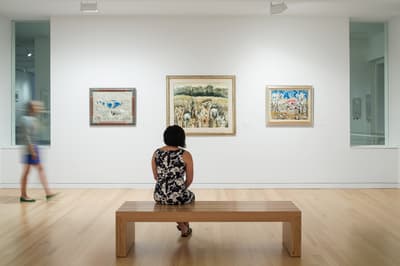 Woman seated on bench looking at three framed works of art.