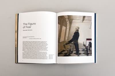 An open book showing text on one page and a painting of a skeleton in a suit sitting on a stool in front of a window on the other.