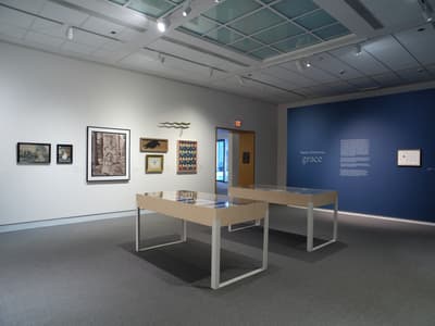 An art gallery with framed artworks on white and blue walls and glass-topped tables in the center.