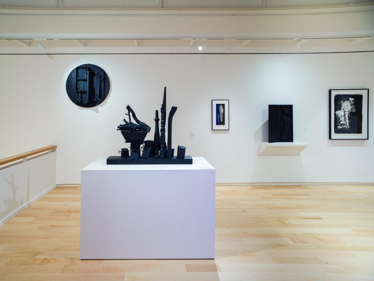 Art gallery with abstract sculptures and framed artworks on a white wall.