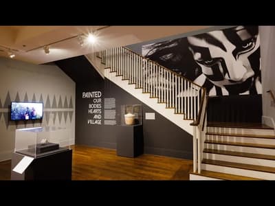 Art exhibition with a staircase, screen, mural, and display pedestals.