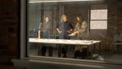 three individuals standing at a conference table reviewing documents