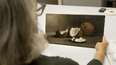 Looking over someone's shoulder holding a work of art with arms outstretched. The work depicts coconuts.