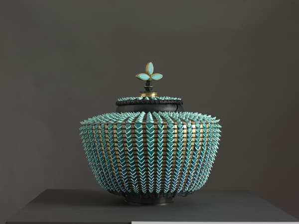 Decorative vessel with a textured, spiky surface and blue accents on a dark background.